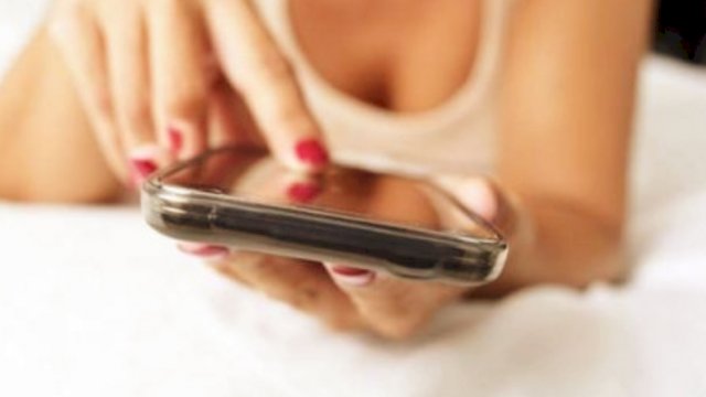 Seseorang yang berpakaian cukup terbuka sambil menggengam smartphone (foto ilustrasi).