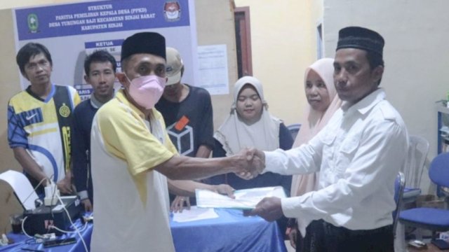 Ketua Panitia Pilkades, Agus Ampa (kiri&mdash;memakai masker) berjabat tangan dengan Calon Kepala Desa Turungan Baji, Sabri (kanan). Minggu (9/1) FOTO: CR/Renaldi